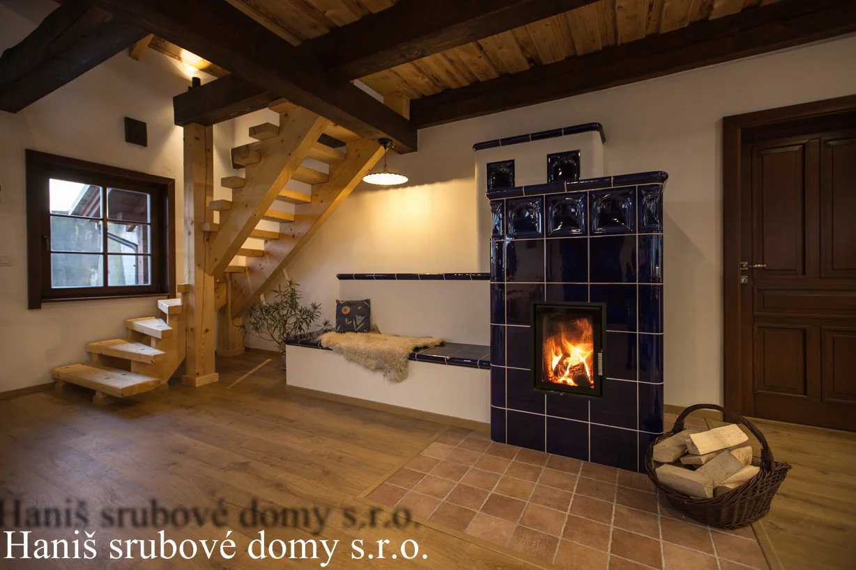 Rohová lavice s ovčí kůží u kachlových kamen a dřevěného schodiště