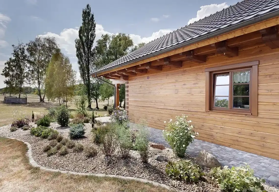 Detail rohu srubového domu s oknem a kamenitým záhonem