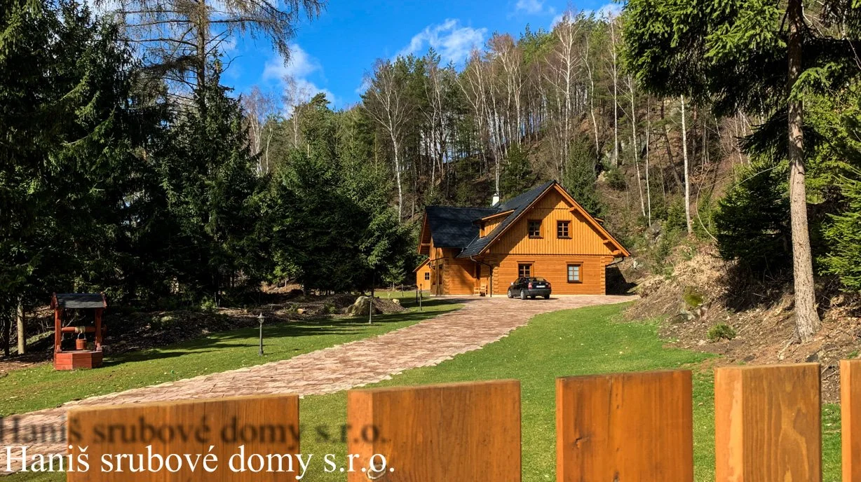 Dřevěný srub v lese s příjezdovou cestou a autem před vchodem